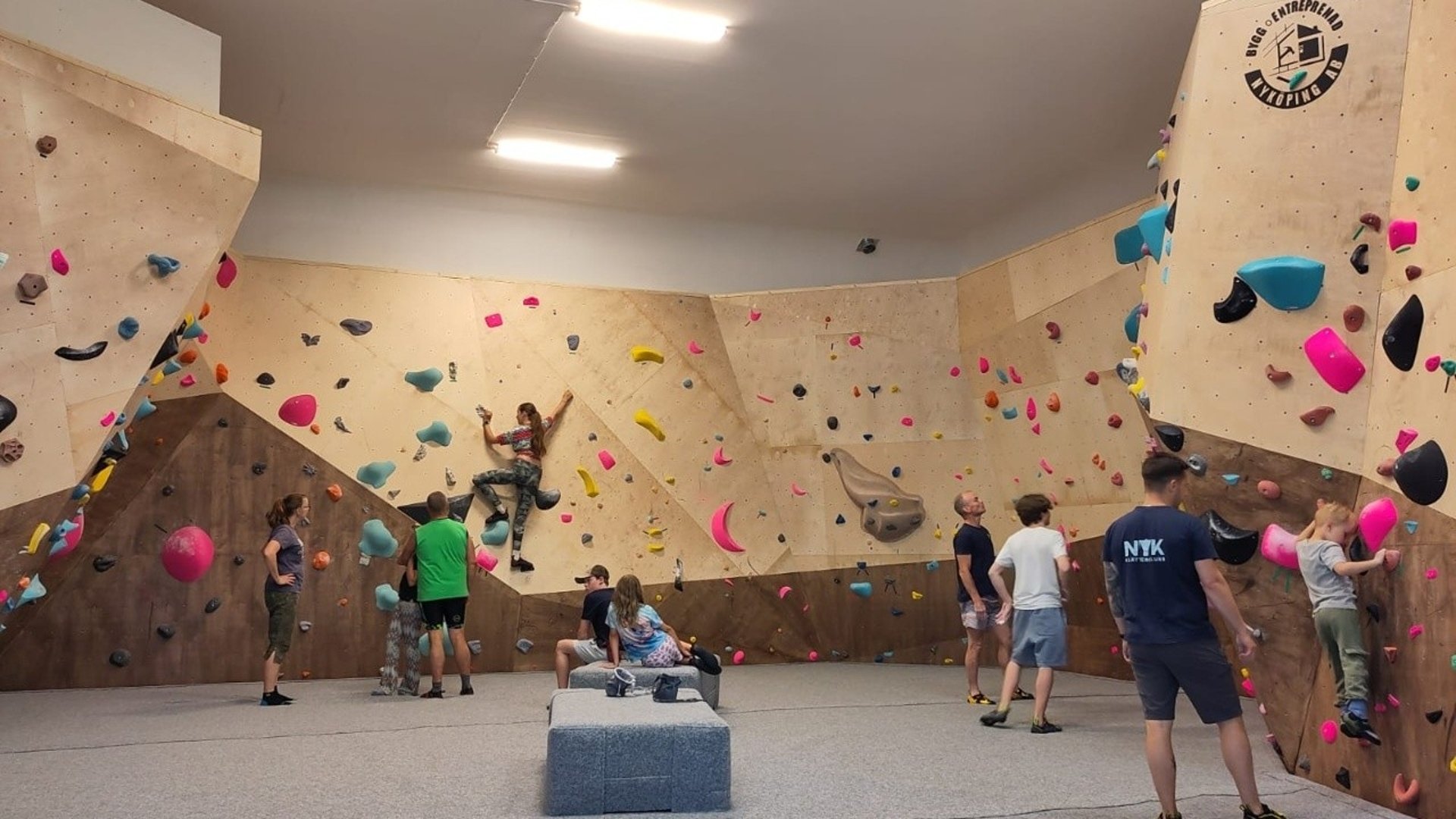 Personer som klättrar inomhus på klätterväggar med mattor under. 