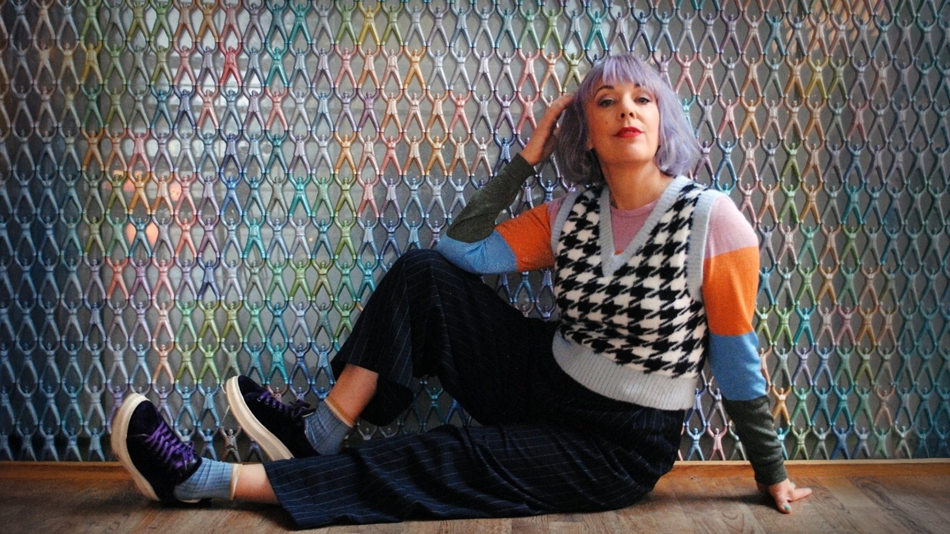 En bild på Marit Bergman sittande på ett golv framför en färgglad vägg.