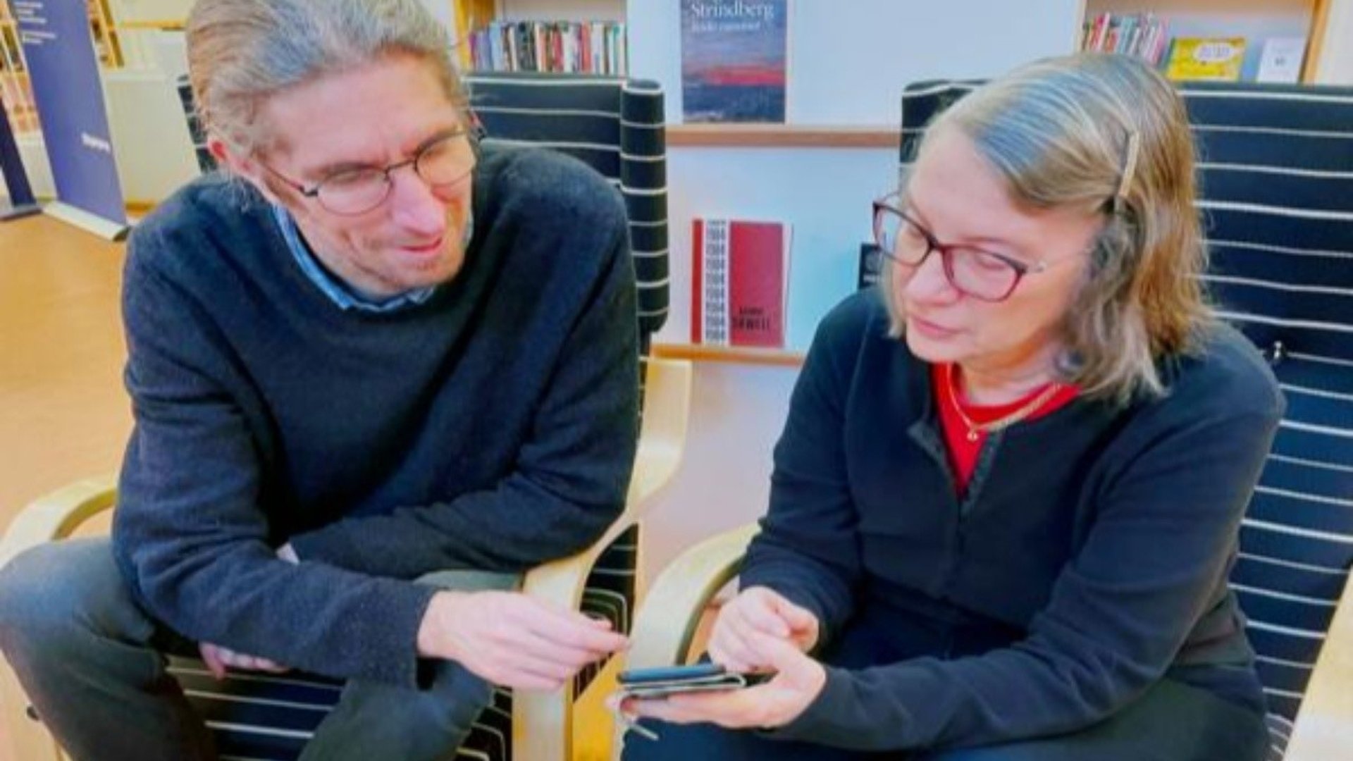 En bibliotekarie hjälper en äldre kvinna med hennes mobil.