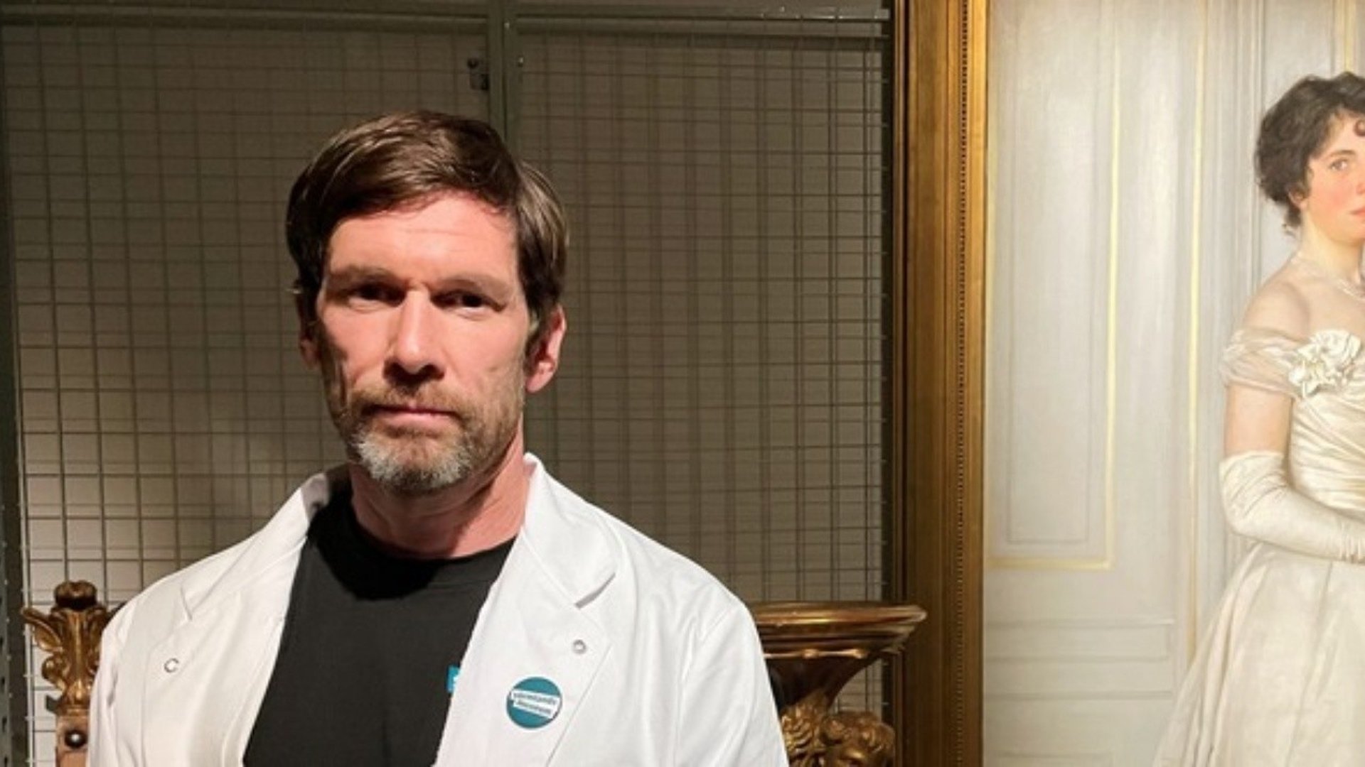 Man i vit rock ser allvarligt in i kameran