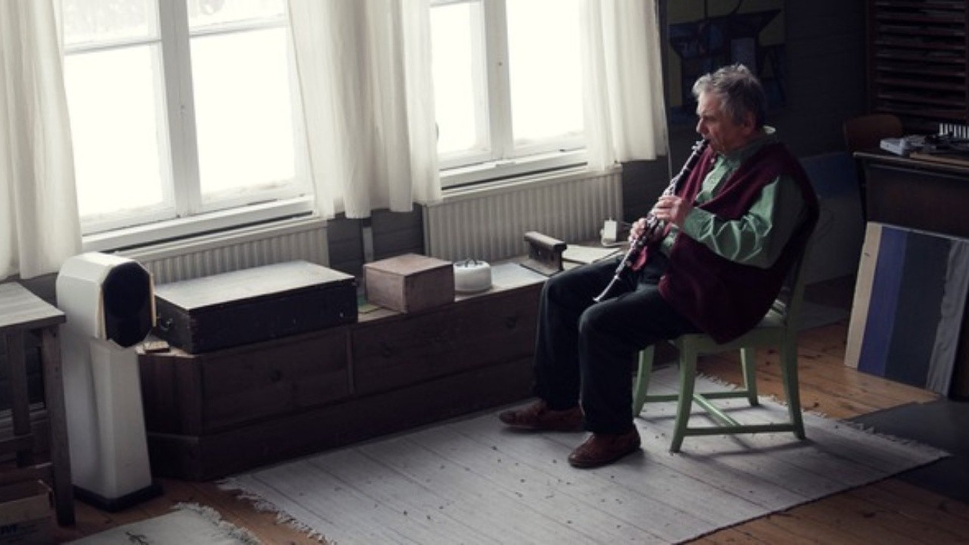 Farbror sitter framför ett fönster o spelar blåsinstrument