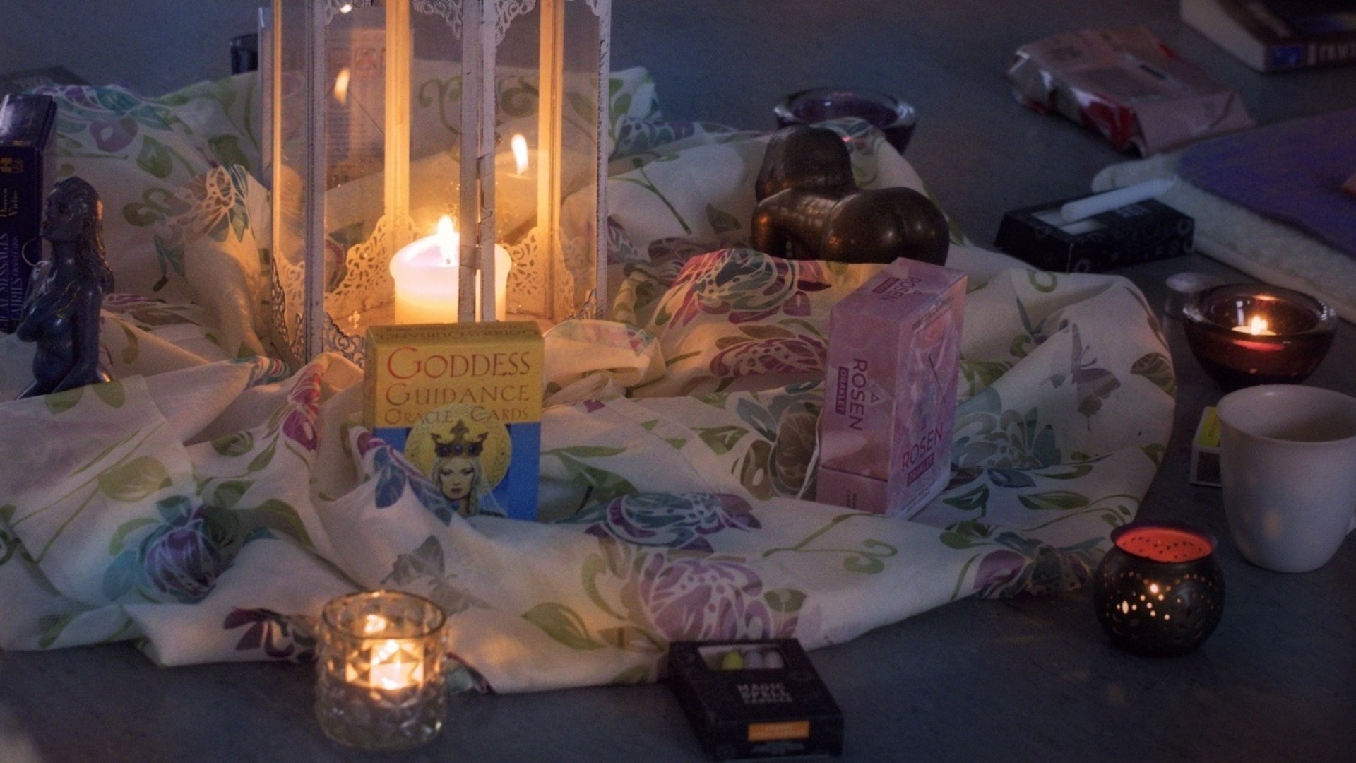 Ljus lykta i mitten av bilden. Tyg under. Mindre ljuslyktor i en ring runt den stora lyktan.