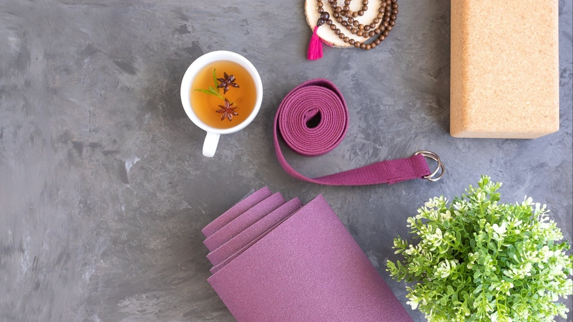 Bild på en del av en yogamatta, ett block, en tekopp, ett skärp, ett mandalahalsband och en blomma. 