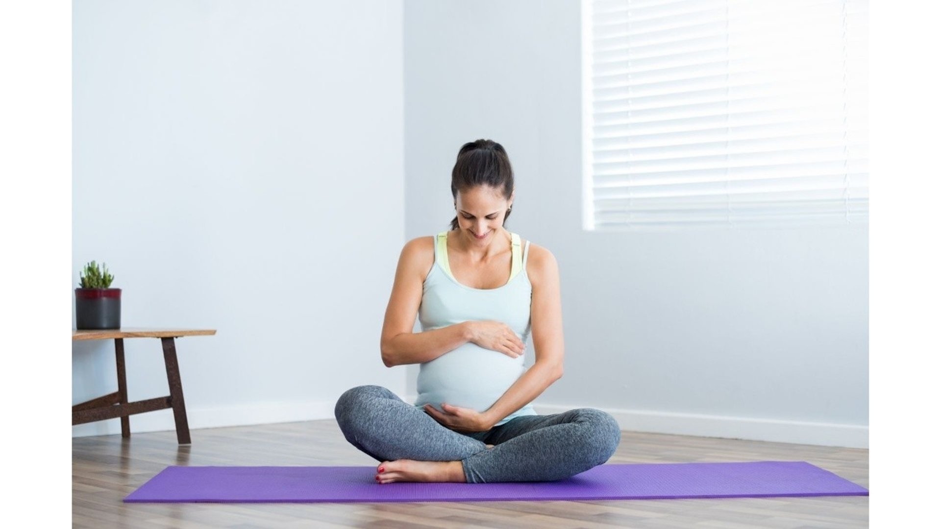 Gravid kvinna sitter på en yogamatta och håller om sin mage.