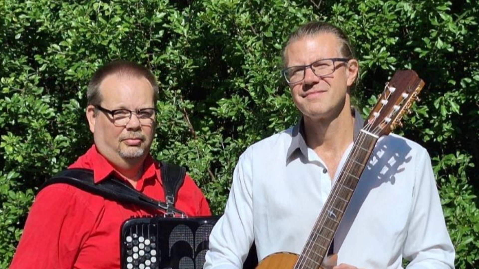 Duo med dragspel och gitarr med sommargröna buskar som bakgrund