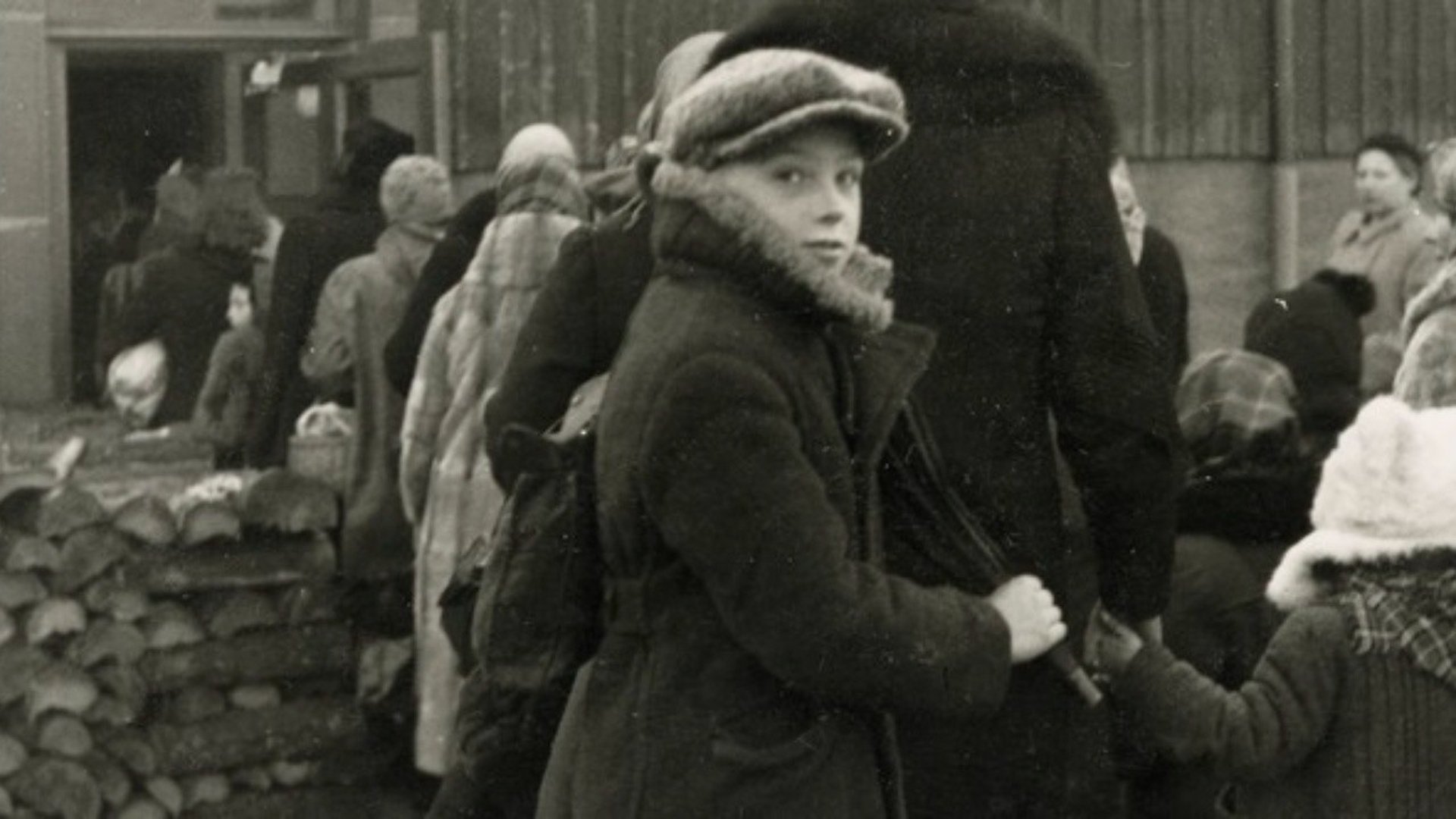 Svartvitt foto på en kö, en pojke vänder sig om mot kameran
