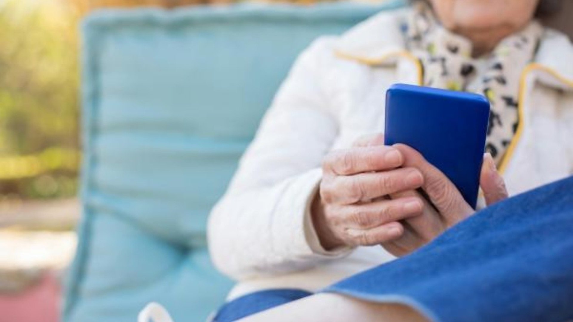 En äldre kvinna sitter med sin blåa mobil.