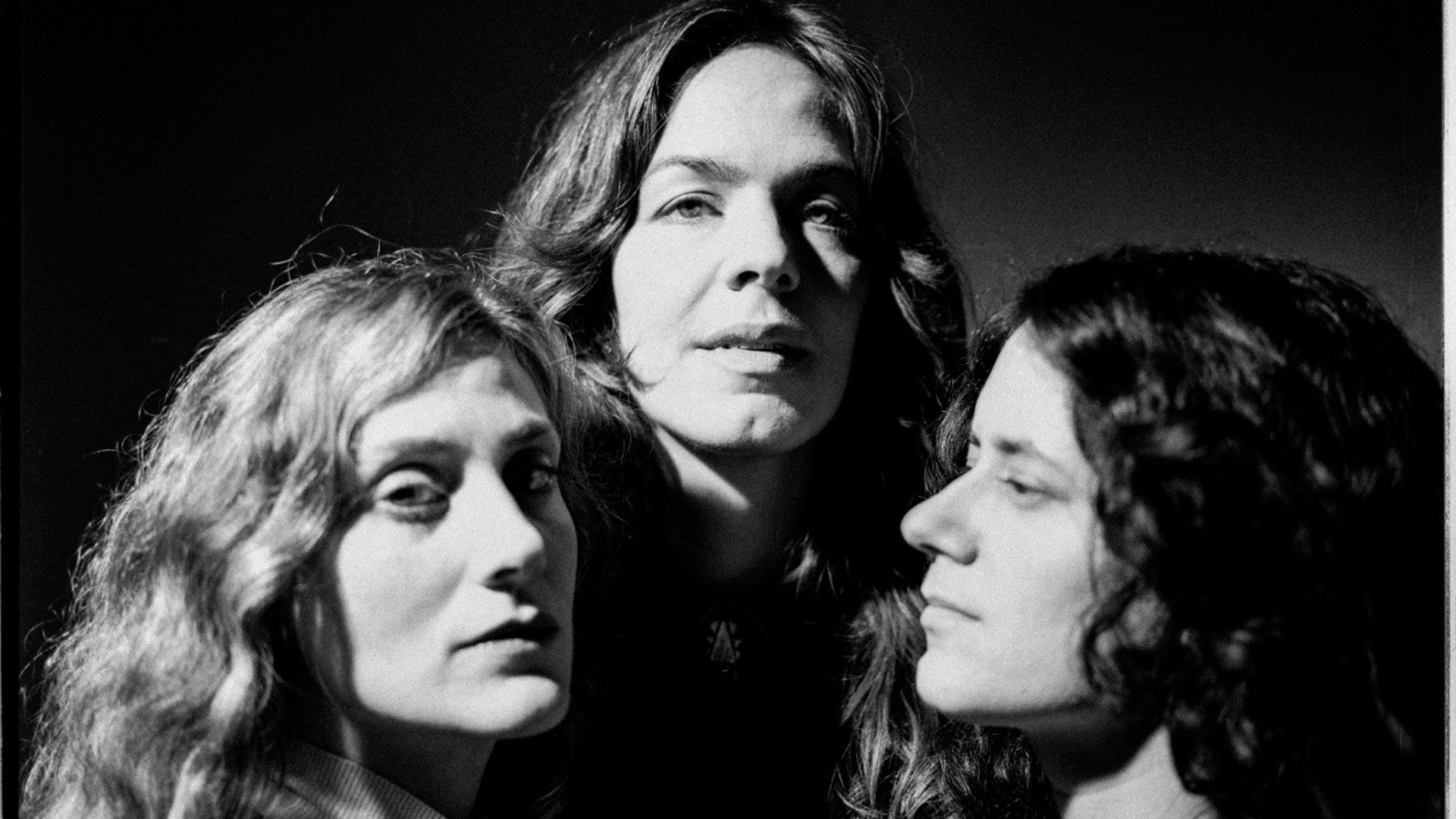 Bild på de tre artisterna. Tre kvinnor med långt lockigt hår.