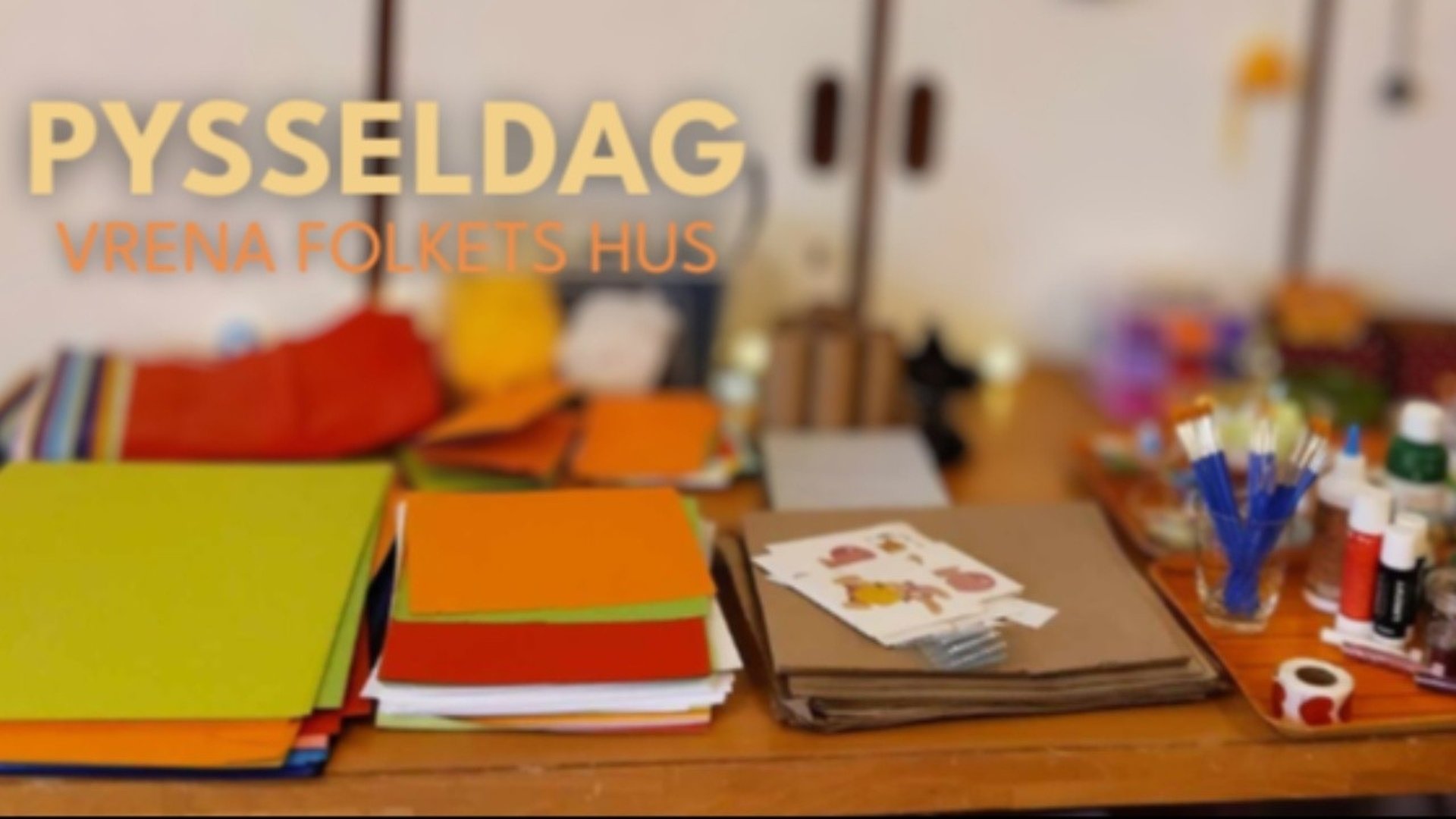Pysselmaterial ligger utspridda på ett bord inomhus i Folkets Hus i Vrena. Färg, penslar, pennor och papper syns tillsammans med målade bilder