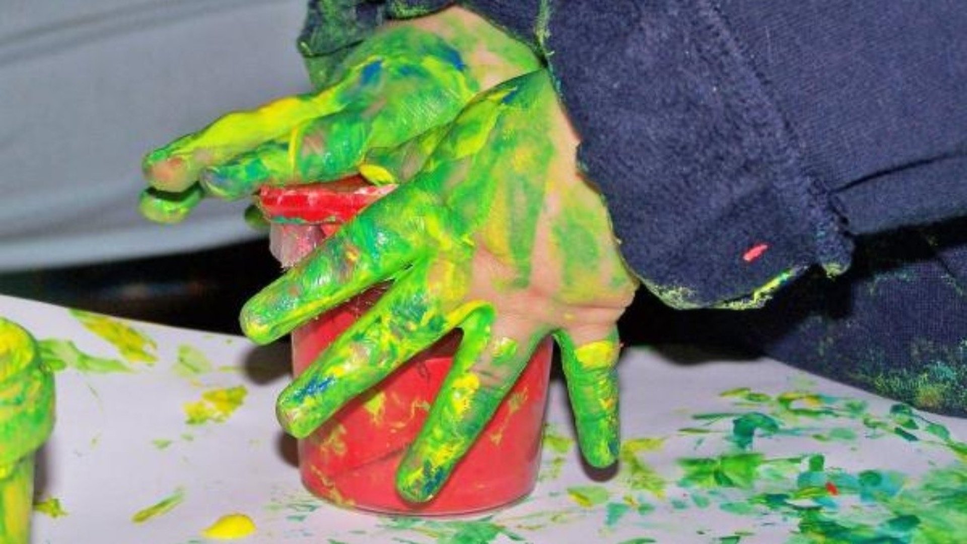 Ett barn med grön färg på händerna bygger en skulptur.