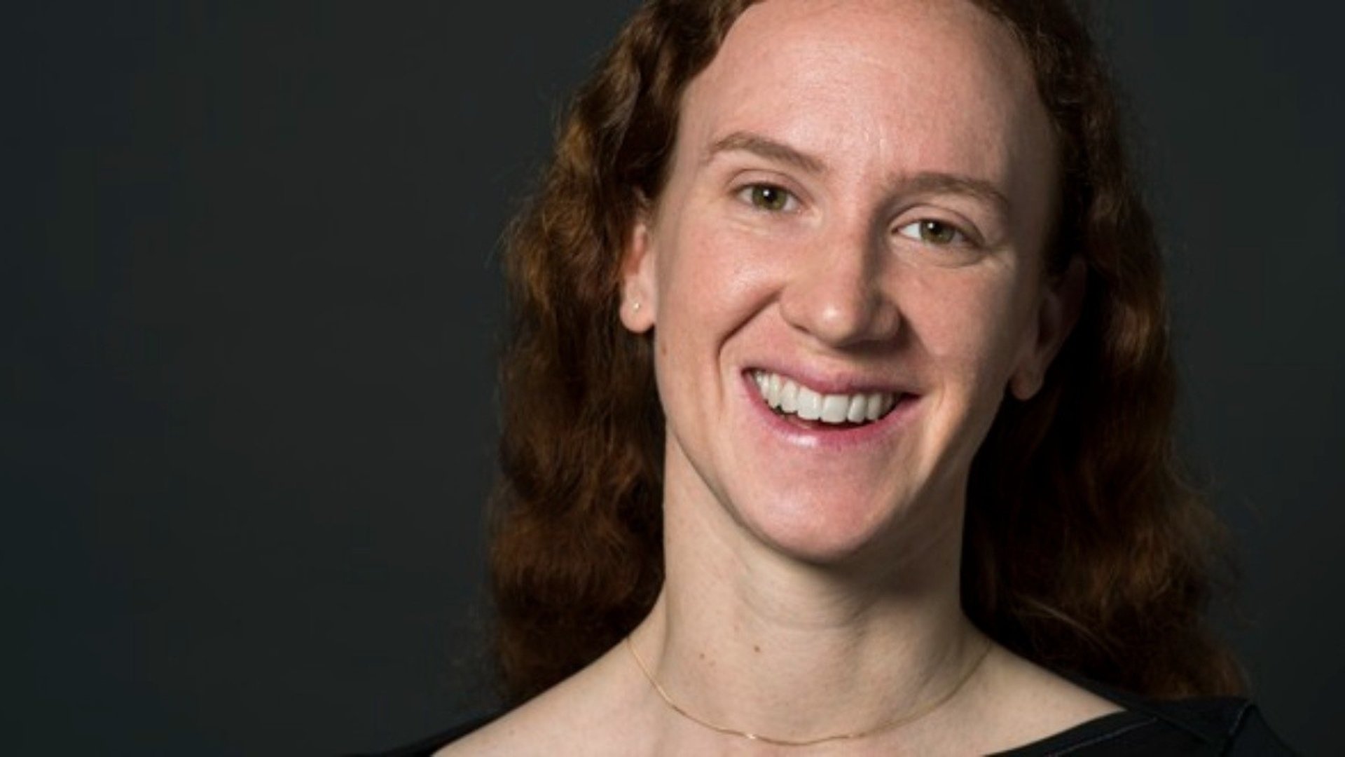 Person med mörkt hår ler in i kameran