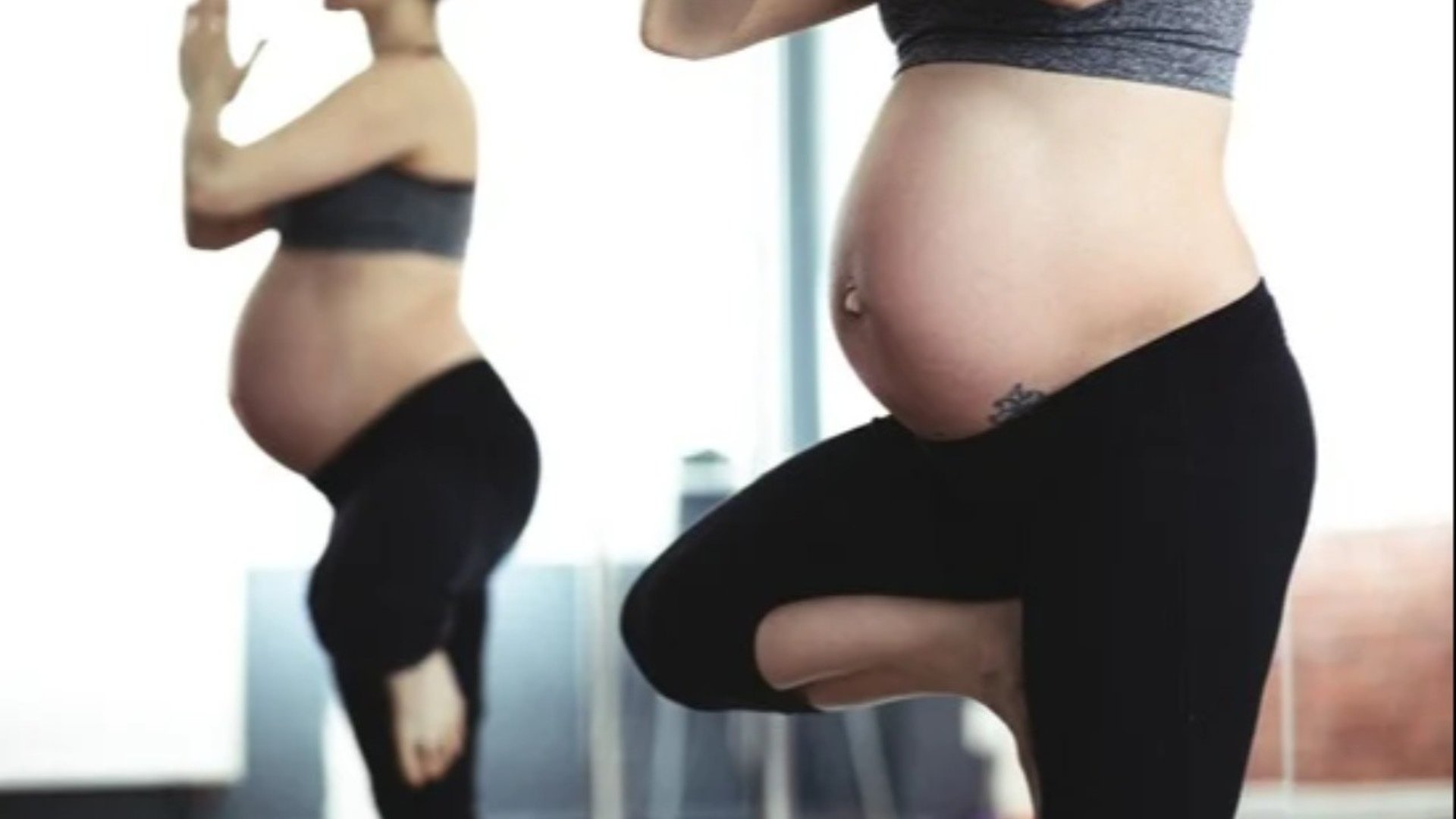 Gravid kvinna som står i en yogaposition. Hennes spegelbild syns i bildens bakgrund.