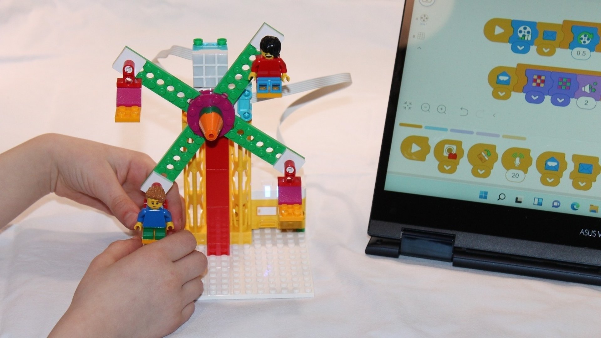 Barnhänder som bygger med lego. På bilden syns även en bärbar dator.