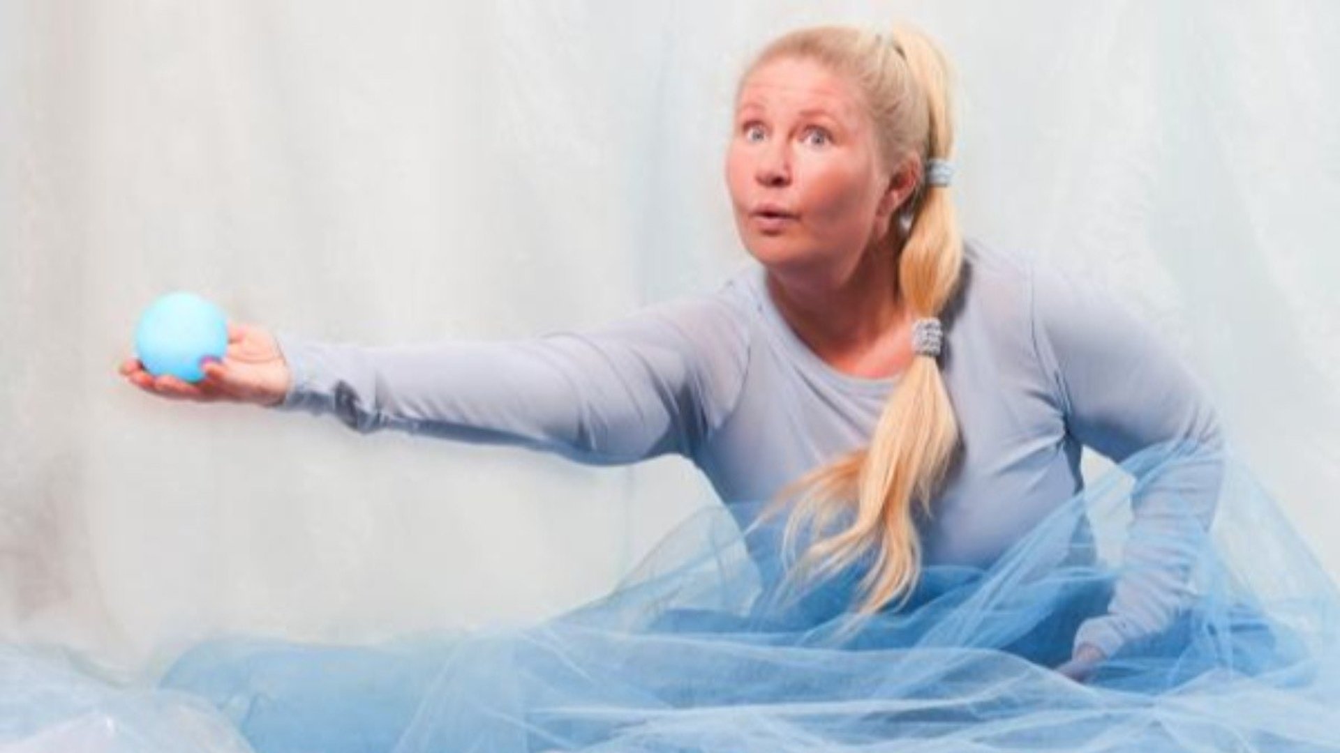 En blond kvinna i ljusblåa kläder dansar med en blå boll.