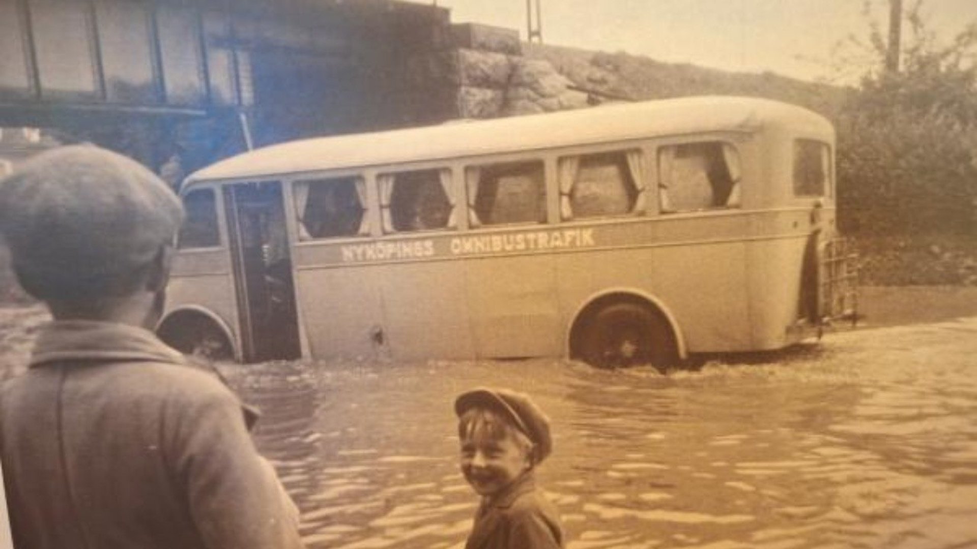 En gammal buss i Nyköping kör på en översvämmad väg.