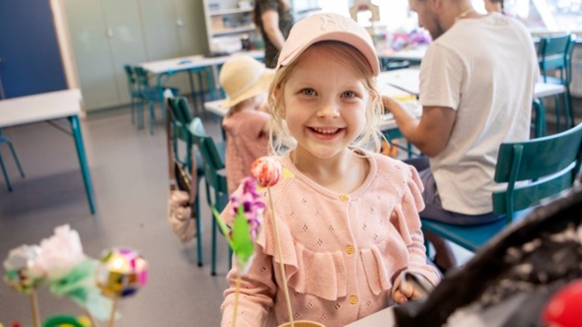 Glad liten flicka i rosa tröja o keps ler in i kameran