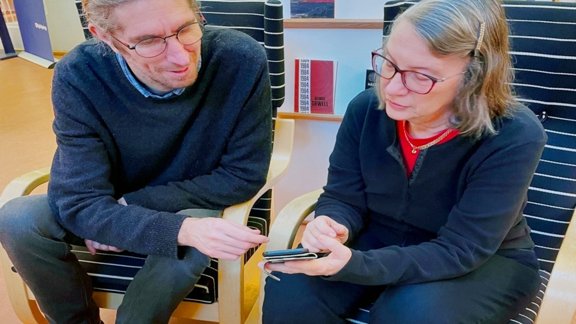 En bibliotekarie hjälper en person med personens mobil.