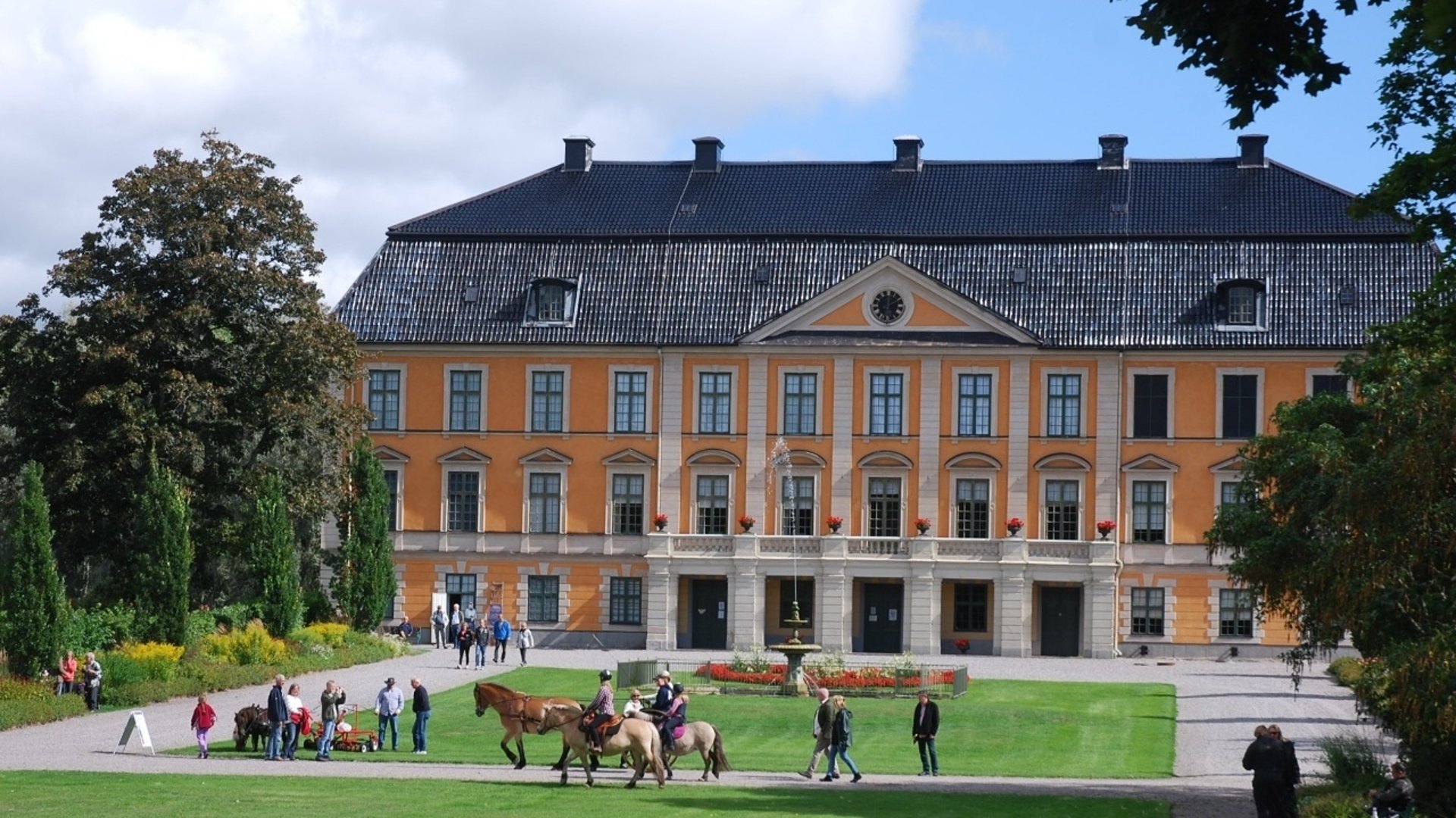 Nynäs slott med hästar och människor i slottsparken.