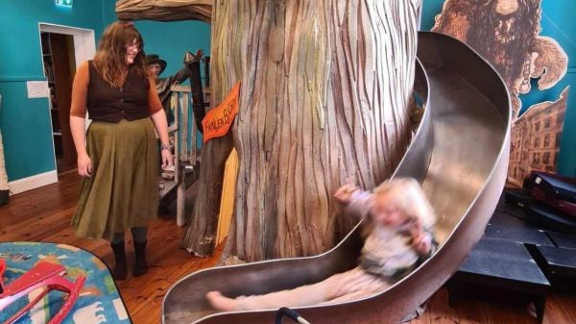 En kvinna tittar på när ett barn åker rutchkana.