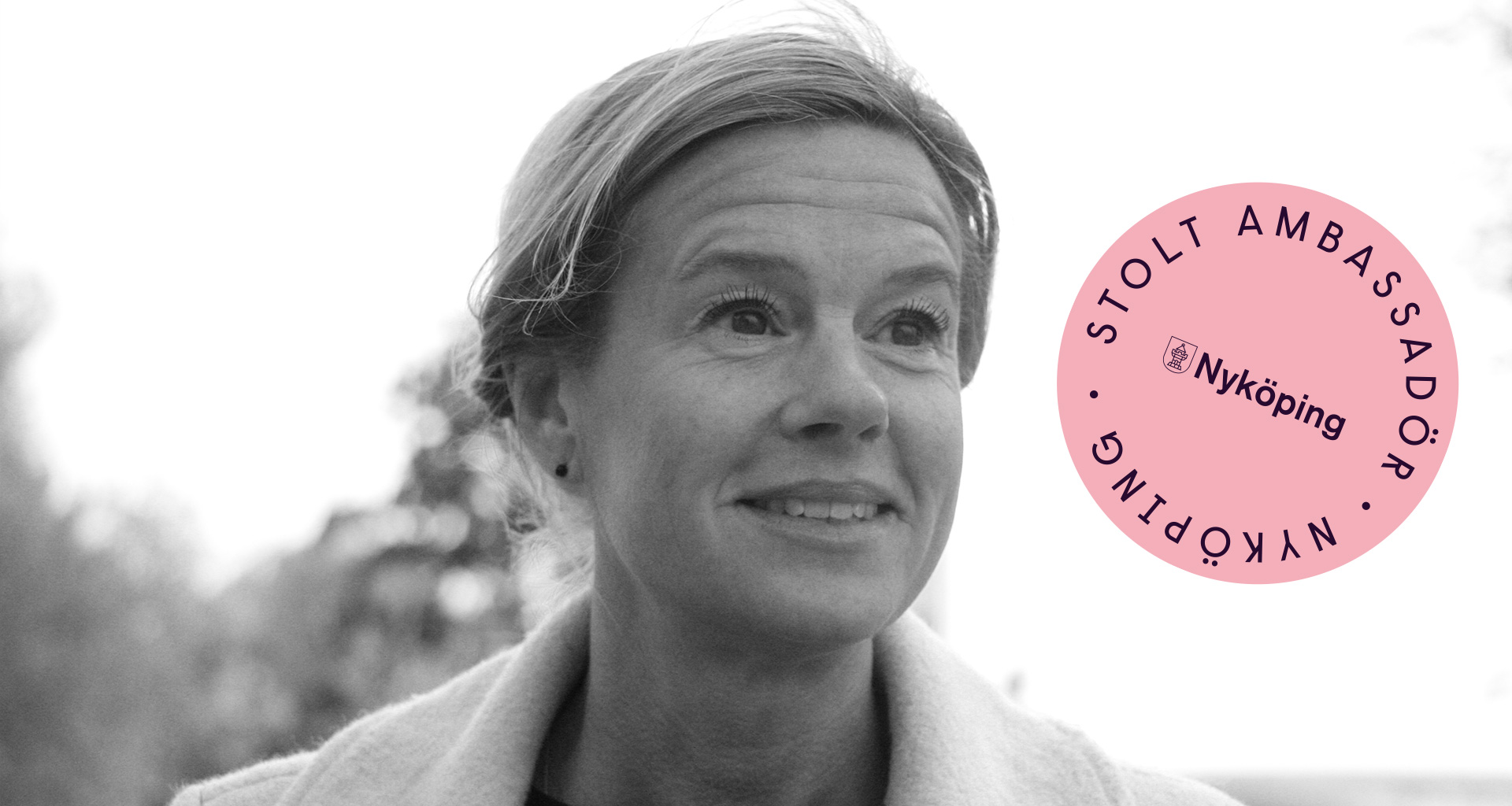 Kvinna  med uppsatt hår. I hörnet syns en rosa cirkel med texten Stolt ambassadör.