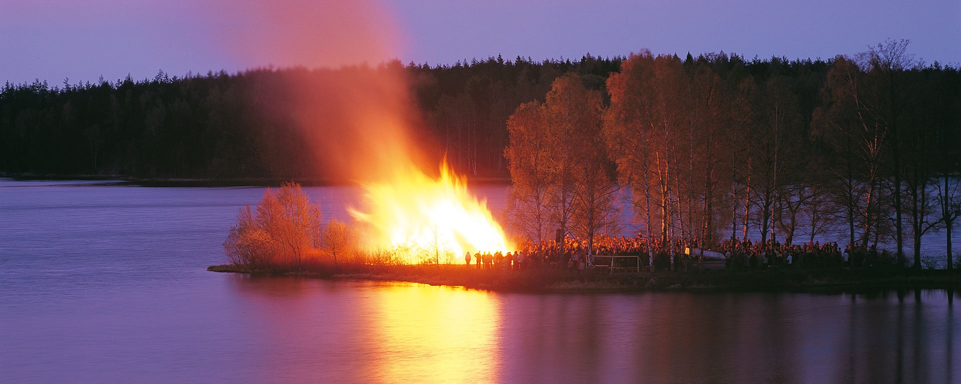 En folkmassa har samlats för att se en majbrasa på en udde.