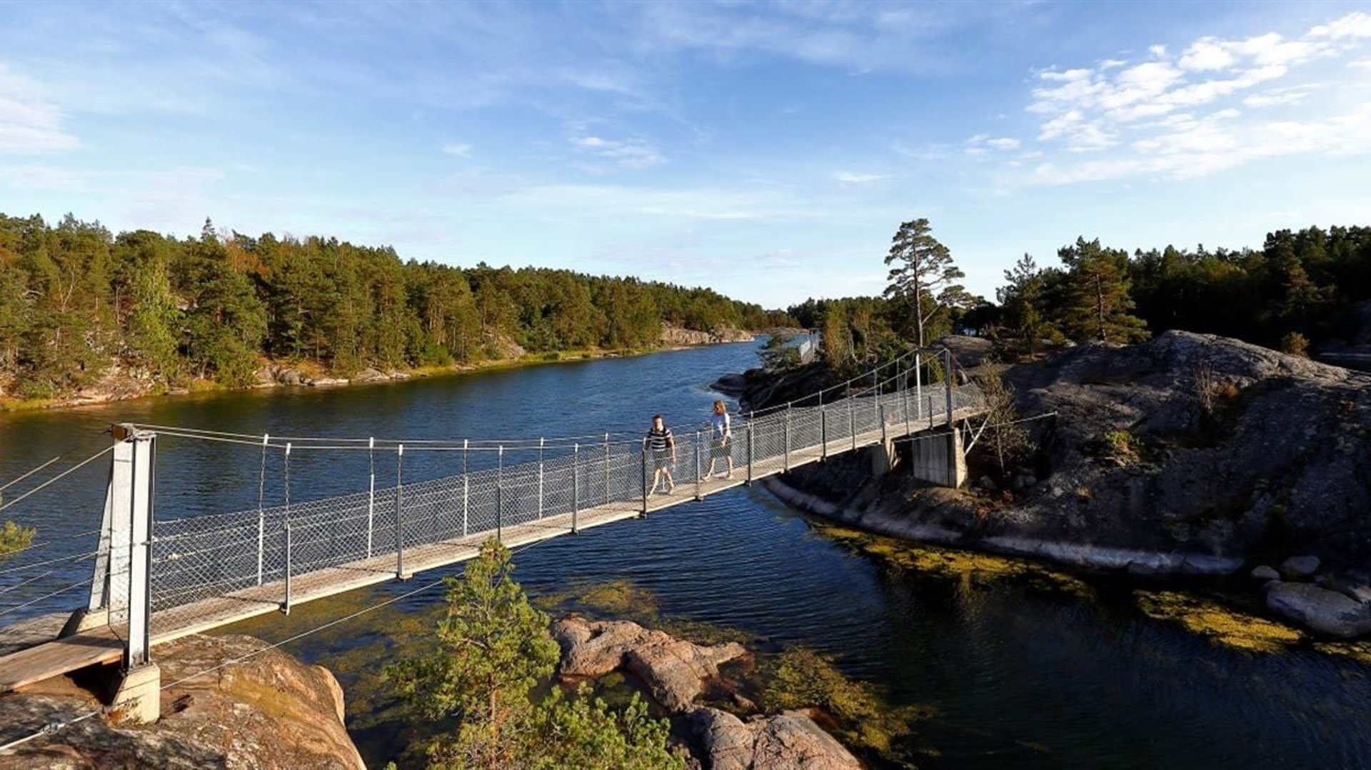 Två personer går över en hängbro en sommardag