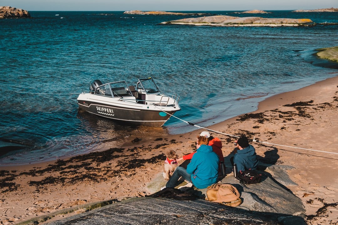 En motorbåt vid en ö och människor som sitter på stranden.