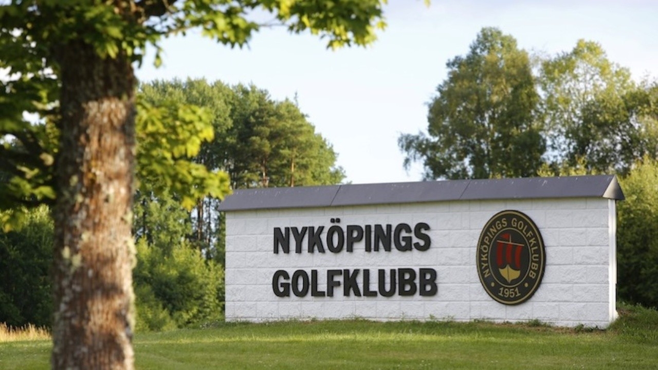 Utomhus skylt med texten "Nyköpings golfklubb" med svart text, logotype och vit bakgrund.