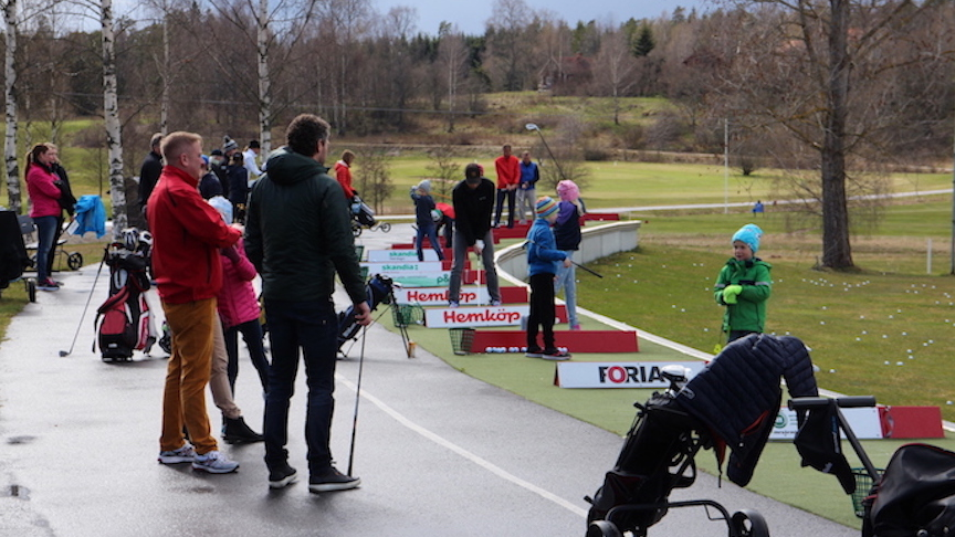 Folk som står och kollar och slår på drivingrangen