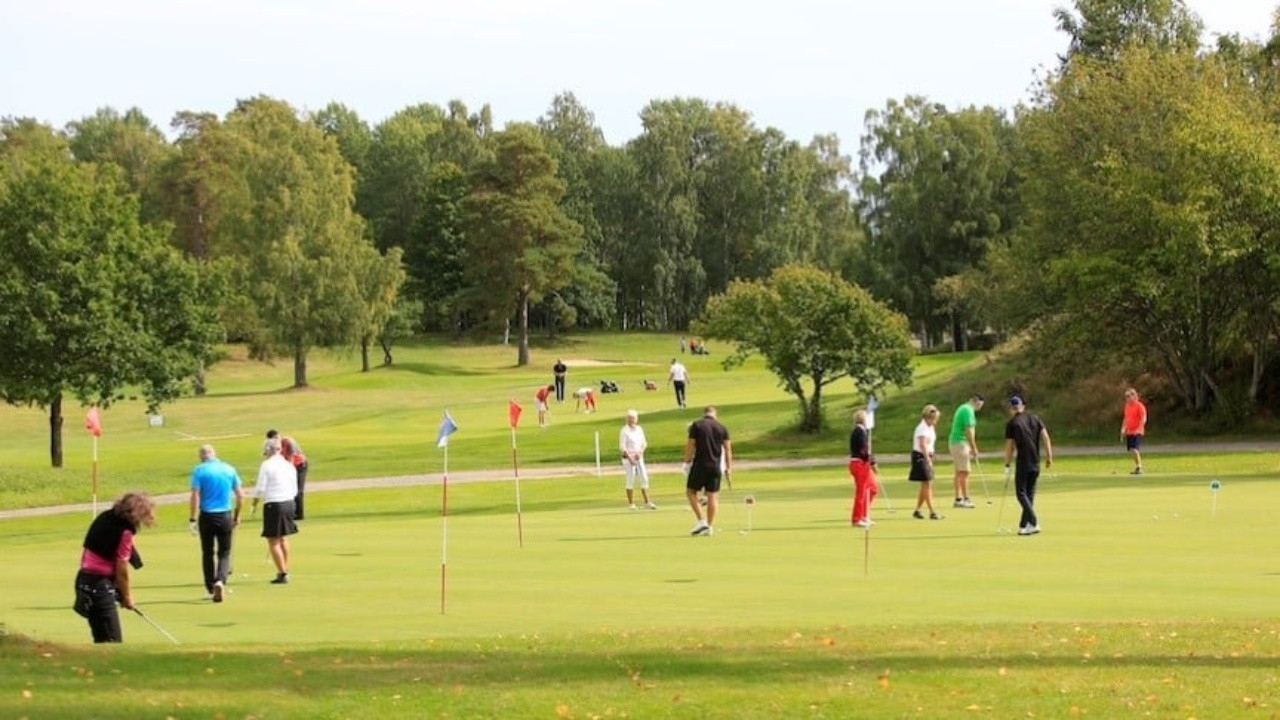 Golfande personer på golfbana med skog i bakgrunden